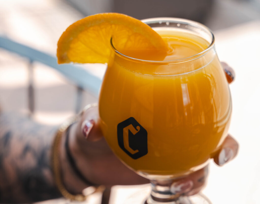 Orange cocktail in a stemmed glass with an orange slice garnish, held by a person.