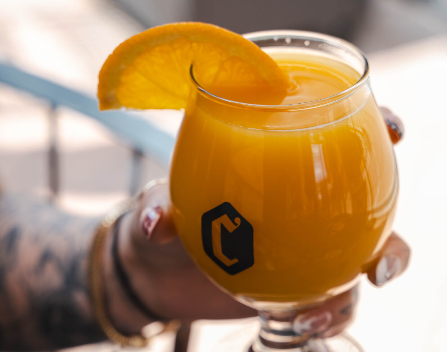 Orange cocktail in a stemmed glass with an orange slice garnish, held by a person.