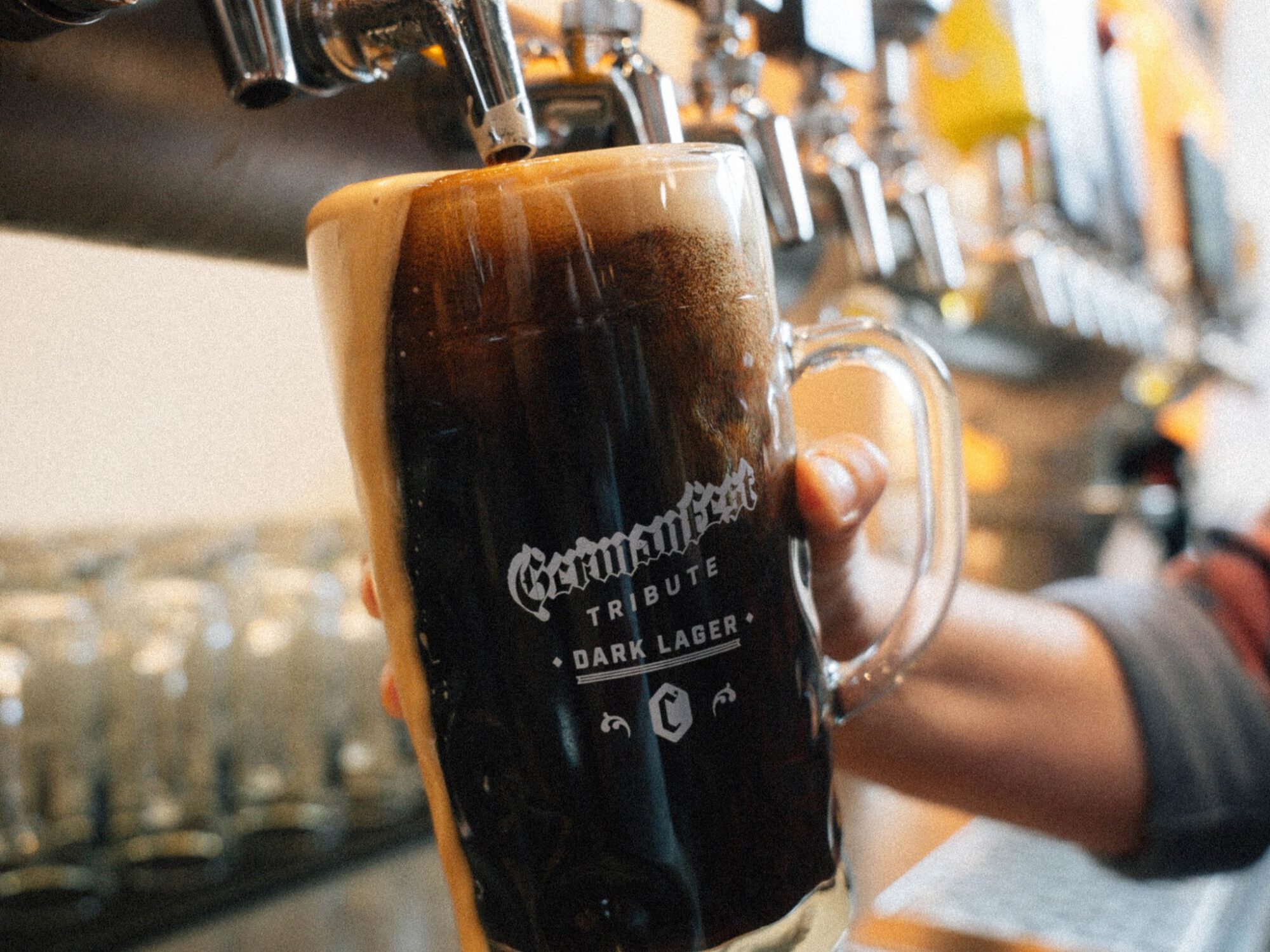 Close-up of a dark stout being poured from a beer tap into a glass mug at a bar or pub setting.