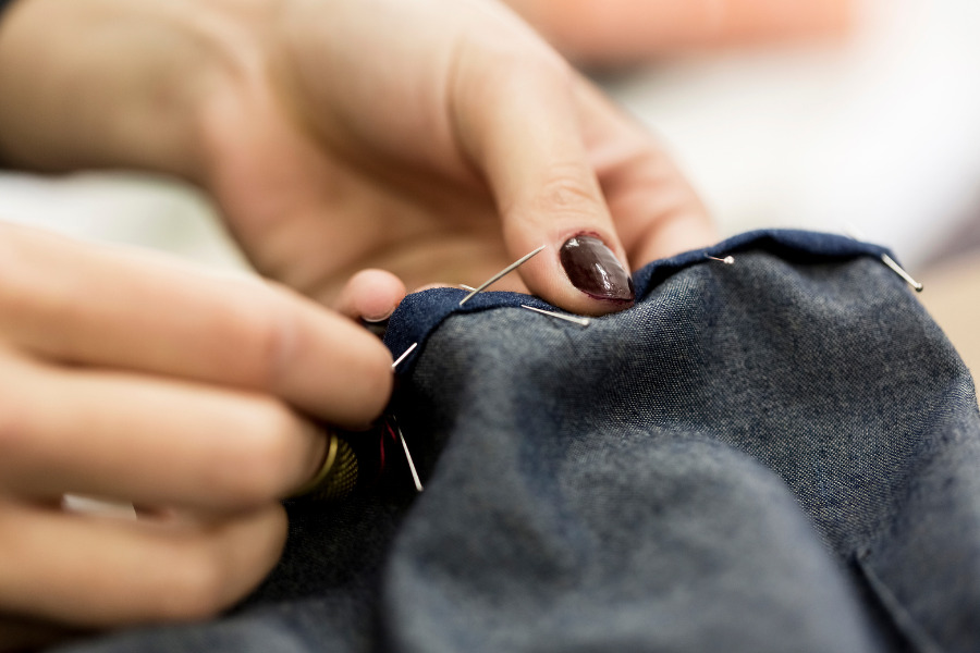 Close-up of hands sewing dark fabric with a needle and thread in motion.